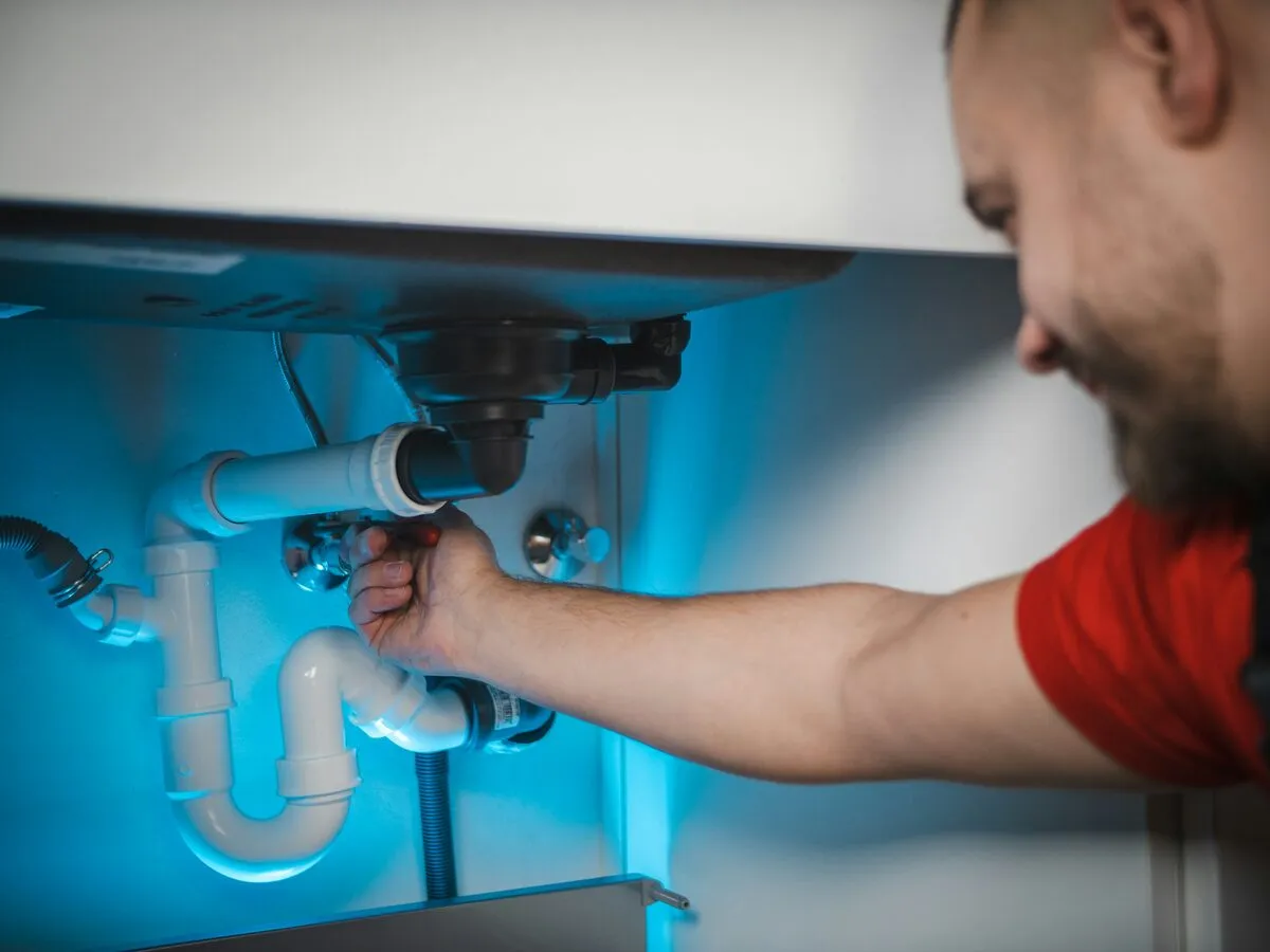 Engineer fitting new waste pipework under a sink