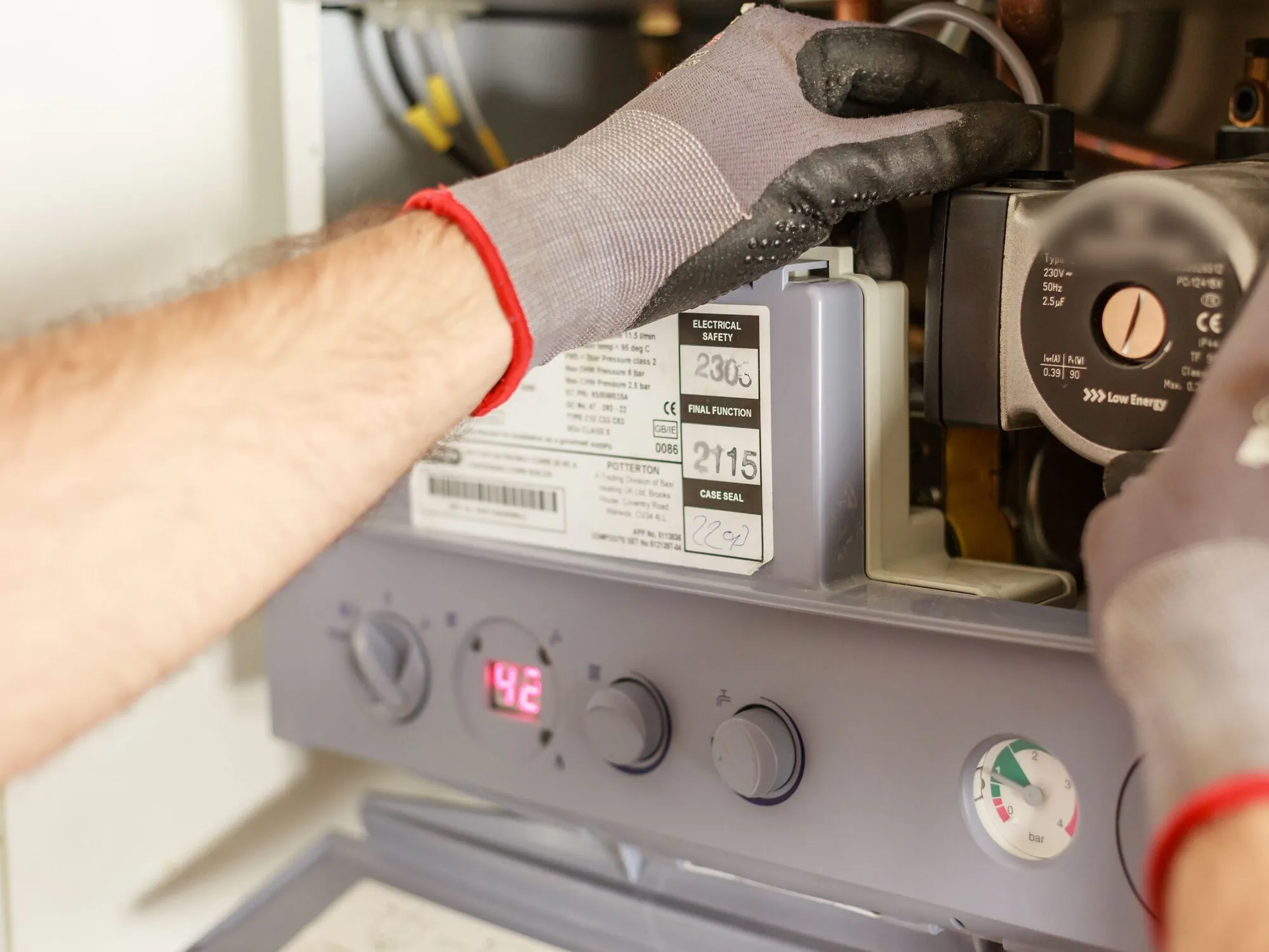 Gloved hands servicing the pump inside an open gas boiler